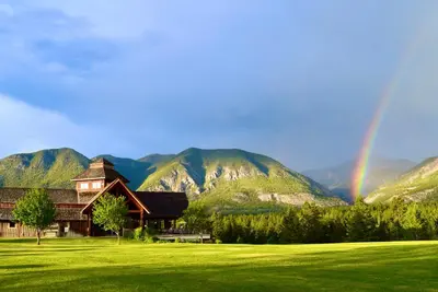 a rainbow over a house with mountains in the background at Headwaters Lodge at Eagle Ranch Resort in Invermere