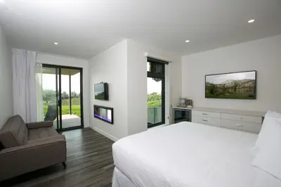a white bedroom with a bed and a chair at The Inn at Therapy Vineyards in Naramata