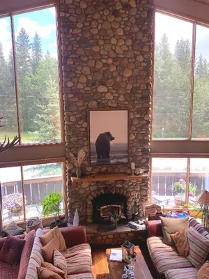 a living room with a stone fireplace with a picture of a bear at Ambleside Lodge Bed & Breakfast in Canmore