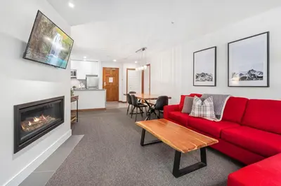 a living room with a red couch and a fireplace at 2BR in The Aspens, Ski In, Ski Out, Pool and Hot Tub, Gas Fireplace, Ski Valet, Gym in Whistler