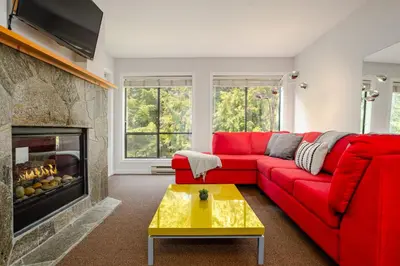 a living room with a red couch and a fireplace at 2BR in Powderhorn, Near Blackcomb, Double-Sided Fireplace, Rooftop Hot Tub, Parking in Whistler