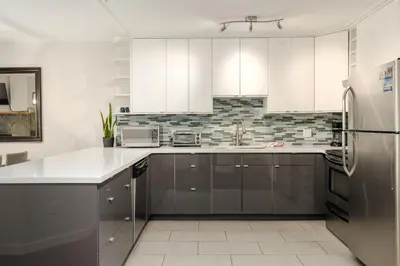 a kitchen with white cabinets and a stainless steel refrigerator at 2BR in Powderhorn, Near Blackcomb, Double-Sided Fireplace, Rooftop Hot Tub, Parking in Whistler