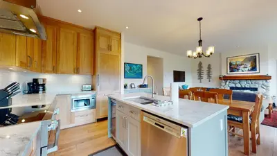 a kitchen with wooden cabinets and a dining room at 2BR in Blackcomb Greens, Wood Burning Fireplace, Communal Hot Tub, Nature Views in Whistler