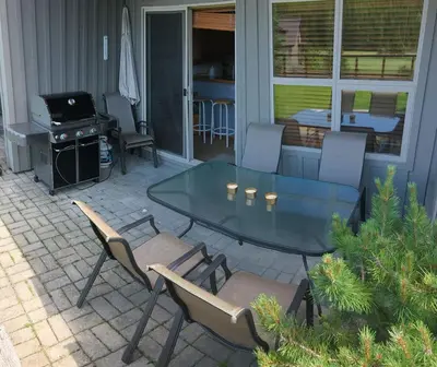 a patio with a glass table and chairs and a grill at 2BR in Blackcomb Greens, Wood Burning Fireplace, Communal Hot Tub, Nature Views in Whistler