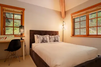 a bedroom with a bed and a desk and windows at Luxury Mountain Retreat with PRIVATE Hot Tub by Harmony Whistler in Whistler