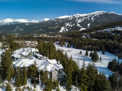 a house covered in snow with mountains in the background at 2BR in The Lynx, Family Sized, Mountain Views, Private Balcony, Tranquil Location, Parking in Whistler