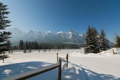 a snow covered field with mountains in the background at BANFF WOODS LODGE in Canmore