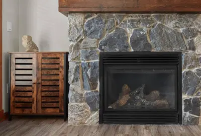 a living room with a fireplace and a stone wall at Newly Renovated Grizzly Lodge, Spacious 3BR 2BA with open pool, hot tub in Canmore