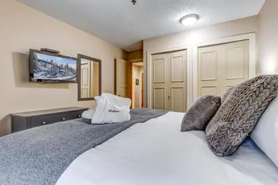 a bedroom with a white bed with a tv on the wall at Greystone Lodge 408 Luxury in Whistler