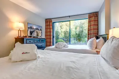 two beds in a room with a large window at Greystone Lodge 226 Ski-in Out in Whistler