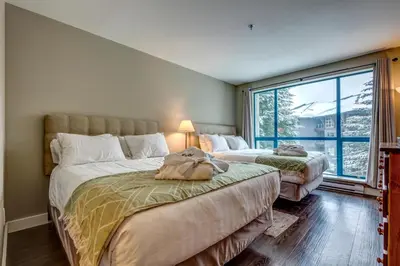 two beds in a room with a large window at Greystone Lodge 221 Ski-in Out in Whistler