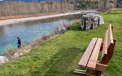 a man standing next to a bench next to a river at Riverside Condos by Fernie Central Reservations in Fernie