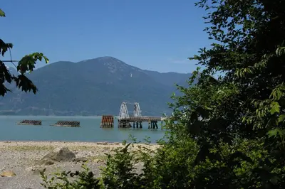 a dock in the middle of a lake with mountains at Porteau Cove Olympic Legacy Cabins in Furry Creek
