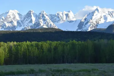 a snow covered mountain range with trees in the foreground at Seven Sisters Mountains House in Kitwanga