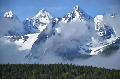 a snow covered mountain with trees and a lake at Seven Sisters Mountains House in Kitwanga