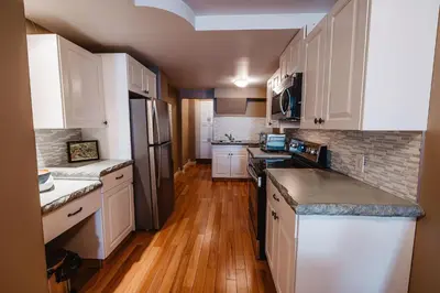 a kitchen with white cabinets and wooden floors at The Watermark Suite - Downtown in Drumheller