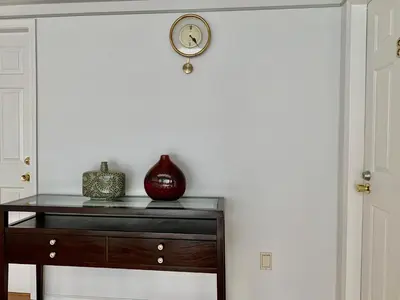 a clock on a white wall next to a dresser at One Bedroom queen bed Sharing Washroom in Tiger Sweet House License## in Richmond