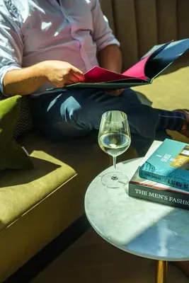 a person sitting on a couch with a glass of wine and a book at The Parker Hotel and Rooftop in Vancouver
