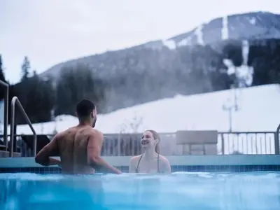 a man and a woman sitting in a swimming pool at Pan Pacific Whistler Mountainside in Whistler