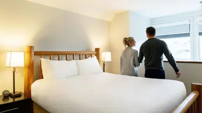 a man and woman standing in a hotel room with a bed at Executive Inn Whistler in Whistler