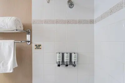 a bathroom with a white tiled wall with three soap dispensers at Executive Hotel Vancouver Airport in Richmond