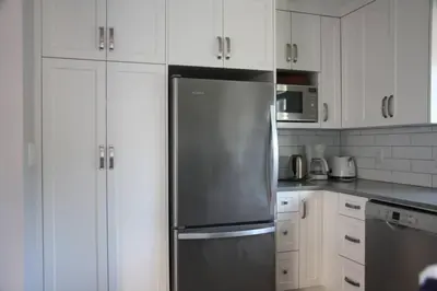 a kitchen with white cabinets and a stainless steel refrigerator at Vancouver Traveller Cottage in Vancouver