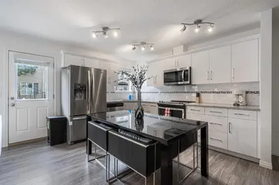 a kitchen with white cabinets and a black counter top at Modern House with Private Backyard & Fireplace in Calgary