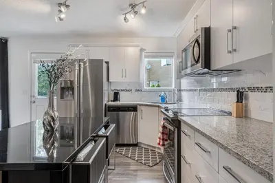 a kitchen with white cabinets and stainless steel appliances at Modern House with Private Backyard & Fireplace in Calgary