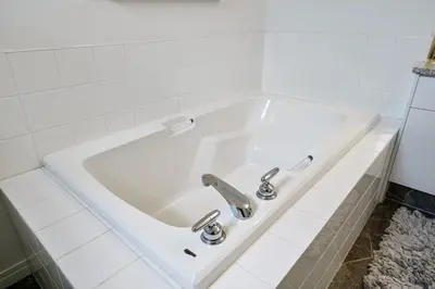 a white bath tub in a white tiled bathroom at Modern House with Private Backyard & Fireplace in Calgary