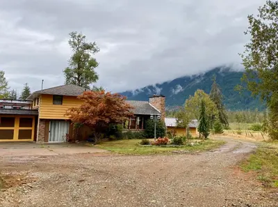 a house on a dirt road in front of a mountain at The Country Barn in Port Alberni