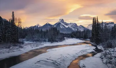 a river in the snow with mountains in the background at Mountain View One Bedroom Vacation Suite - WindTower 119 in Canmore