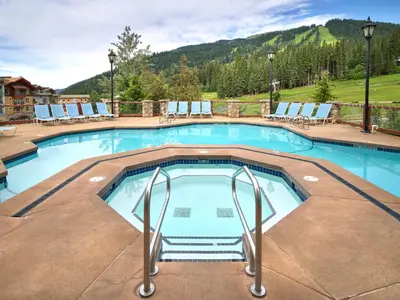 a swimming pool at a resort with chairs and a mountain at Sun Peaks Grand Hotel & Conference Centre in Sun Peaks