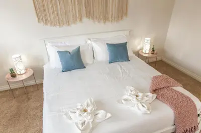 a white bed with blue pillows and white flowers on it at Mediterranean Retreat - King Bed - Fireplace - Garage in Edmonton