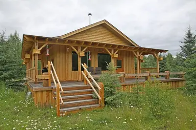 a wooden cabin in a field with a porch and stairs at LDR Lodge - Last Dollar Ranch in Smithers