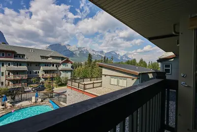a balcony with a view of a pool and mountains at Mtn View Escape with King Size Bed with Outdoor Pool - Banff Pass Included! in Canmore