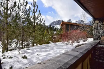 a snow covered yard with a house and mountains at Luxurious Rundle Cliffs Lodge in Spring Creek in Canmore