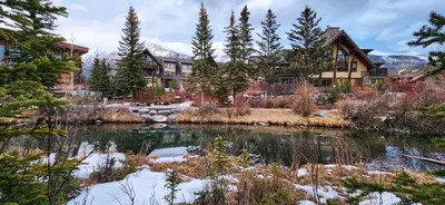a house in the mountains with a pond in front at Luxurious Rundle Cliffs Lodge in Spring Creek in Canmore