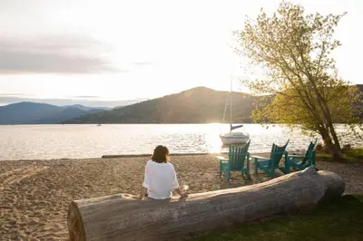 a woman sitting on a log next to a lake at Top Floor on Okanagan Lake with AC & Heated Pool in Vernon