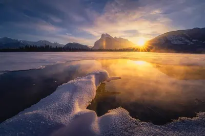 a reflection of the sun in the water with snow at Skyline Escape - Mountain Views - Hot Tub - Pool in Canmore
