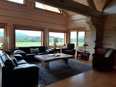 a living room with couches and a table and windows at Jollymore Ranch in Smithers