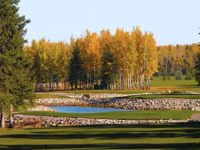 a golf course with a pond and trees at Mountain View Inn & Suites in Sundre