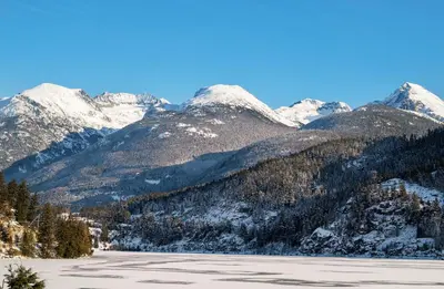 a snow covered mountain range with a lake in the foreground at 2BR in Painted Cliff, Ski In, Ski Out, Communal Hot Tub, Wood Burning Fireplace, Free Parking in Whistler