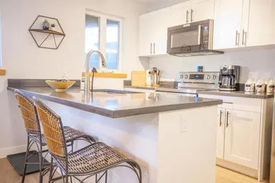 a kitchen with a sink and a counter with two chairs at Storm Bay, Modern 1 Bed Suite and Chefs Kitchen in Ucluelet