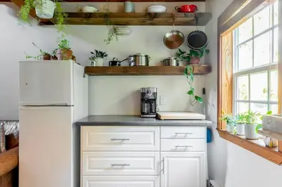 a kitchen with white cabinets and a refrigerator at Fern Gully, Coastal Bohemian Loft at Beach in Ucluelet