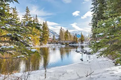 a body of water with trees and snow on the shore at Canmore Cabin by Canadian Rockies Vacation Rentals in Canmore
