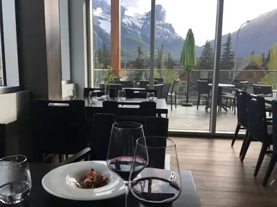 a restaurant with a plate of food and wine glasses at Alluring Mountain View Condo - Right In The Heart Of Downtown - managed by Little Sister Getaways in Canmore