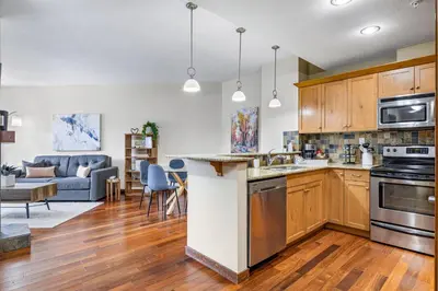 a kitchen with wooden cabinets and a living room at Alluring Mountain View Condo - Right In The Heart Of Downtown - managed by Little Sister Getaways in Canmore