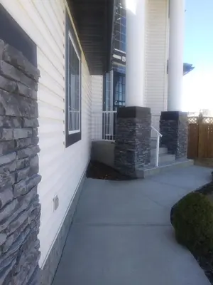 a house with a stone wall next to a sidewalk at Mountain Calm & Private Ensuite Hosted by Maureen in Calgary