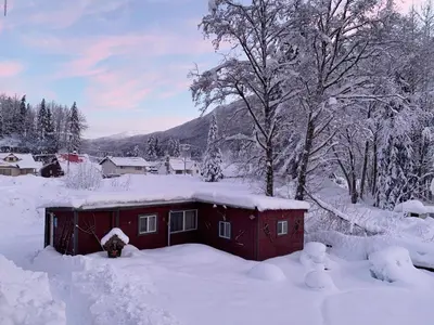 a red cabin in the snow with snow covered trees at The Cabin in Stewart