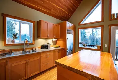 a kitchen with wooden cabinets and a sink and two windows at Stoke Cabin by Revelstoke Vacations in Revelstoke